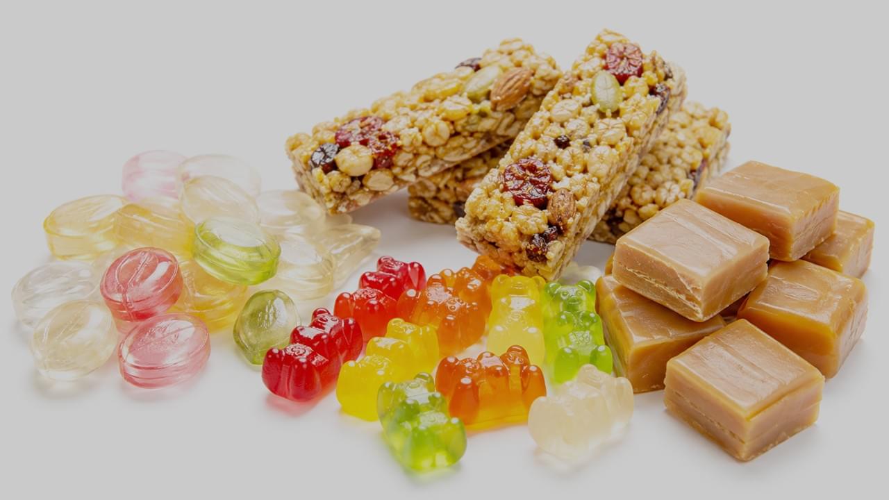 Anwendungen von Süßwaren aus Reissirup, darunter kristallklare Bonbons, zähe Fruchtgummis, Müsliriegel und cremige Karamellprodukte, professionell fotografiert.